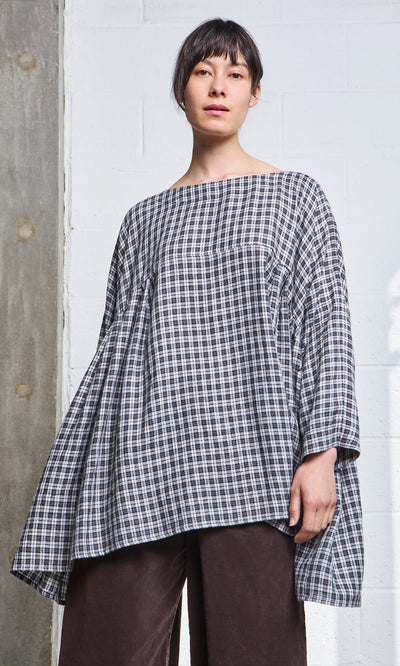Plümo- Woman wearing the Kelli Blouse - Plaid with wide sleeves and dark brown pants, standing indoors.