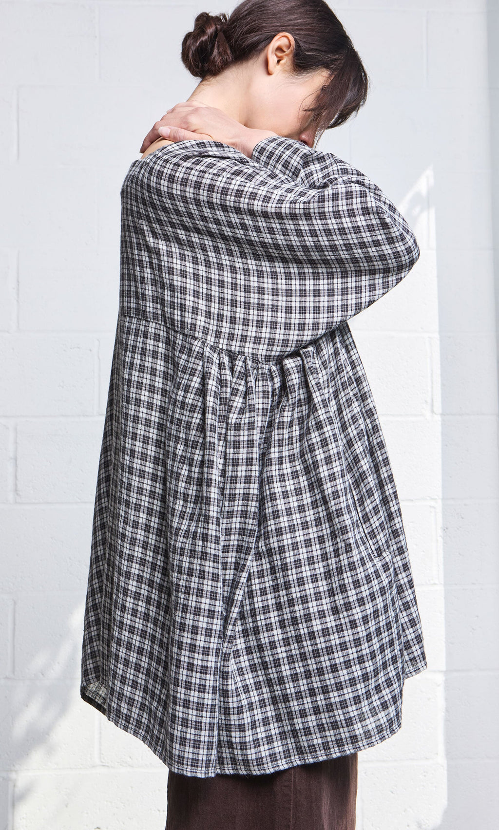 Plümo- Model wears the Kelli Blouse - Plaid, standing sideways with head down and hands resting on their shoulders.