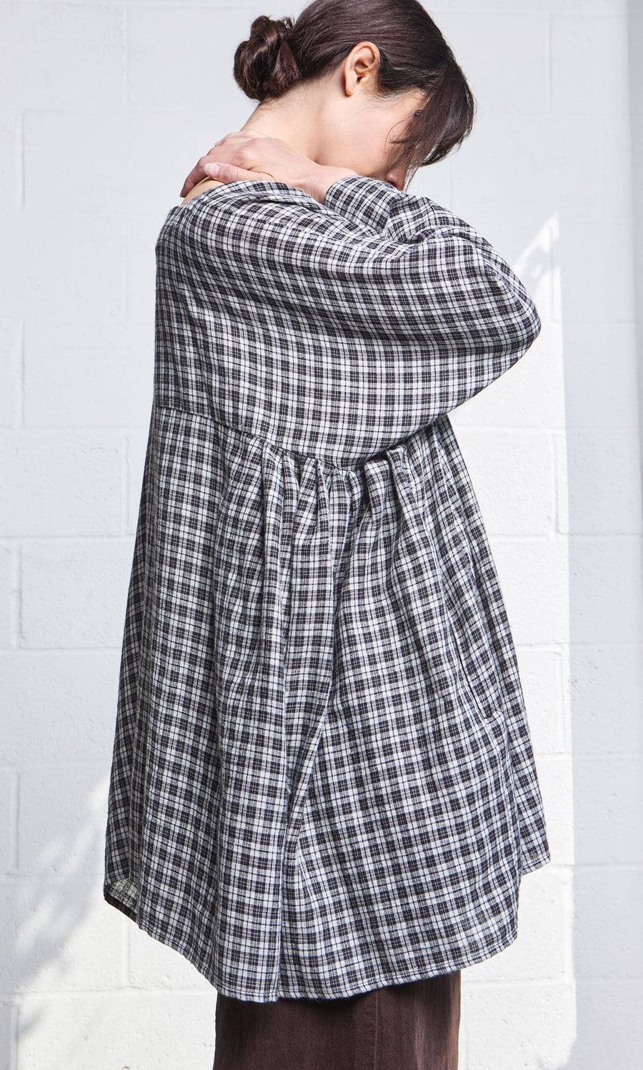 Plümo- Model wears the Kelli Blouse - Plaid, standing sideways with head down and hands resting on their shoulders.