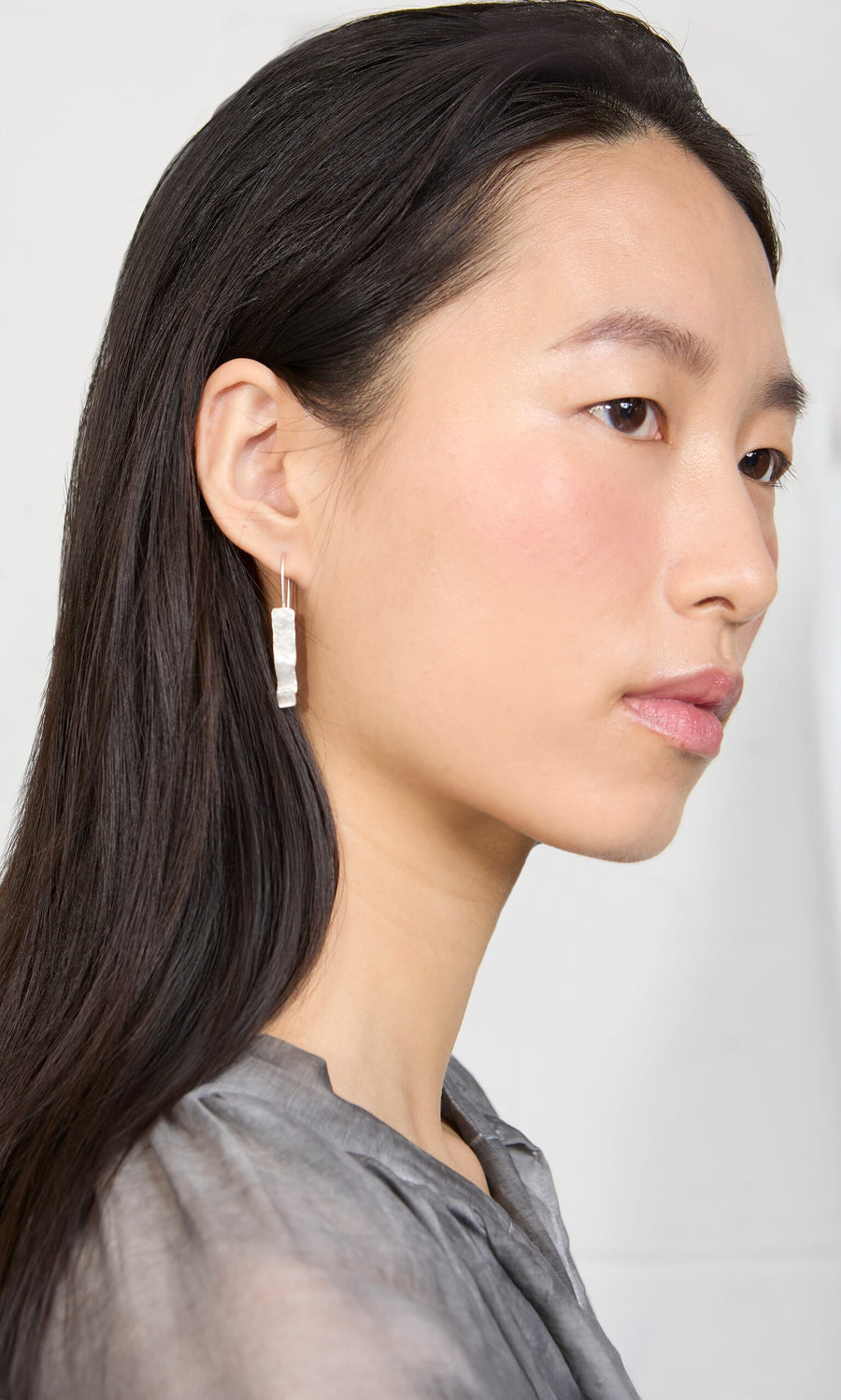 Plümo- Woman with long dark hair in a gray top wears Kenan Earrings, shown in profile against a plain background.