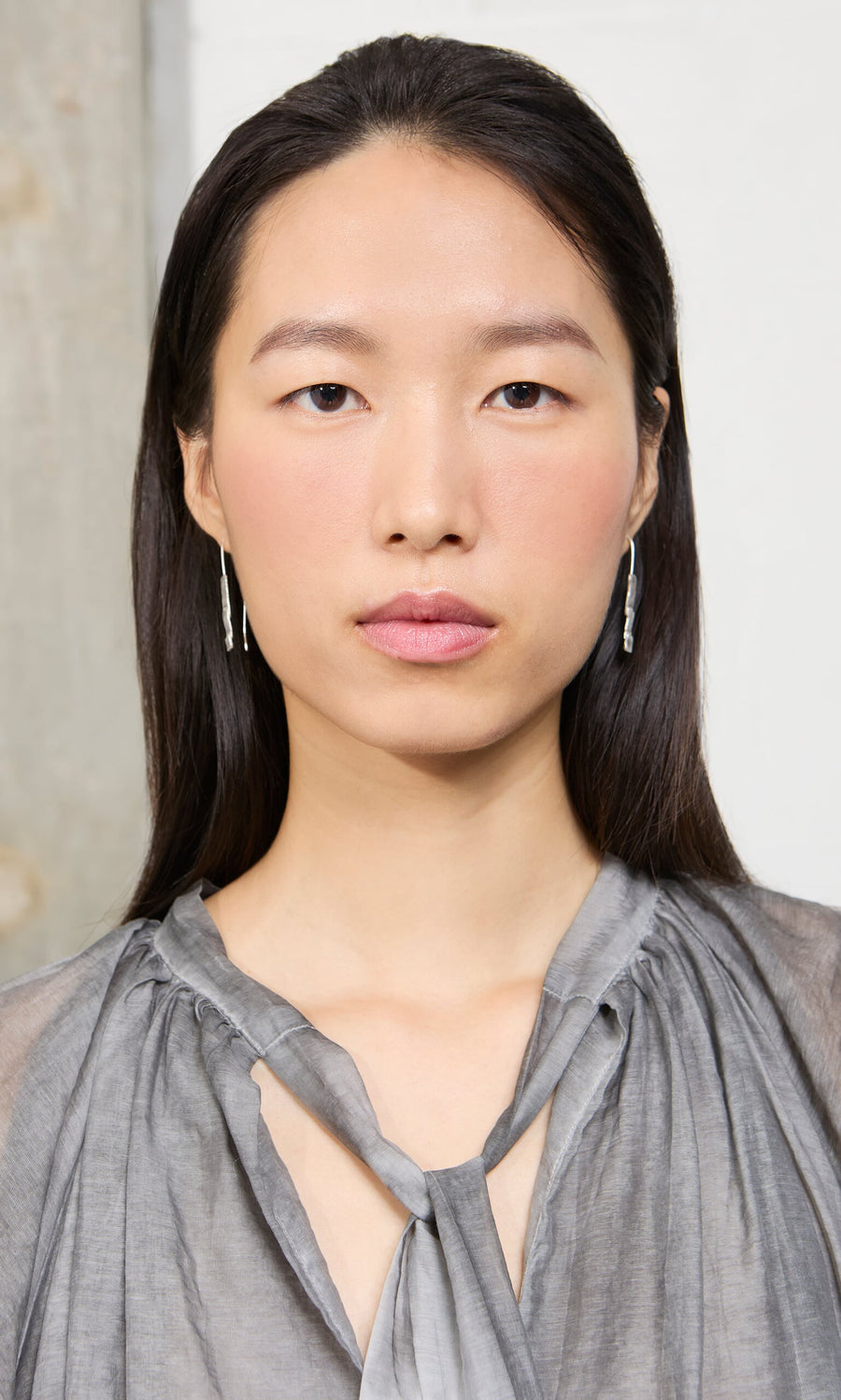 Plümo- Woman with long dark hair, in a gray blouse and Kenan Earrings, looks directly at the camera.
