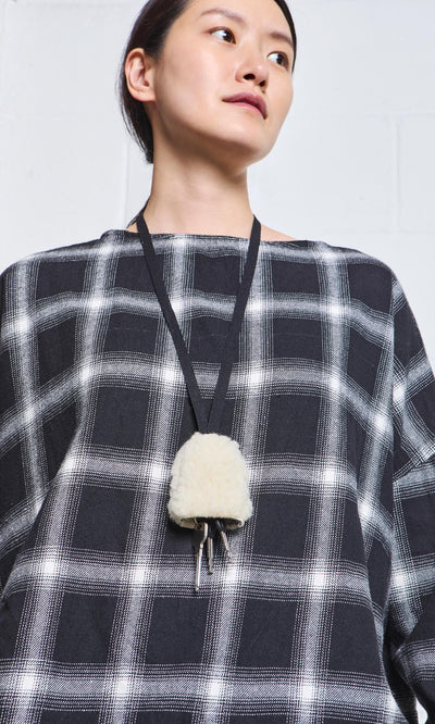 Plümo- Person wearing a black and white plaid top with a Shearling Keyholder necklace, looking slightly to the side.