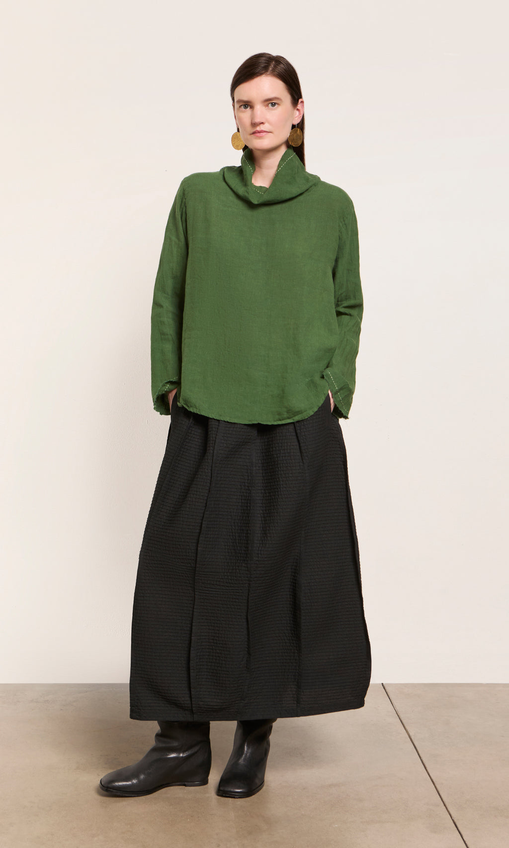 Plümo  Woman wears Kim Ruffle Stitch Blouse, wide black skirt, black boots, and gold earrings against a plain background.