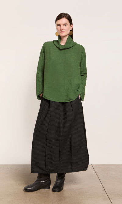 Plümo  Woman wears Kim Ruffle Stitch Blouse, wide black skirt, black boots, and gold earrings against a plain background.