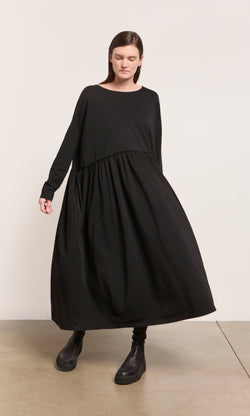 Plümo  Woman in the Kobke Dress and boots stands on a beige floor, embodying effortless Danish design style.