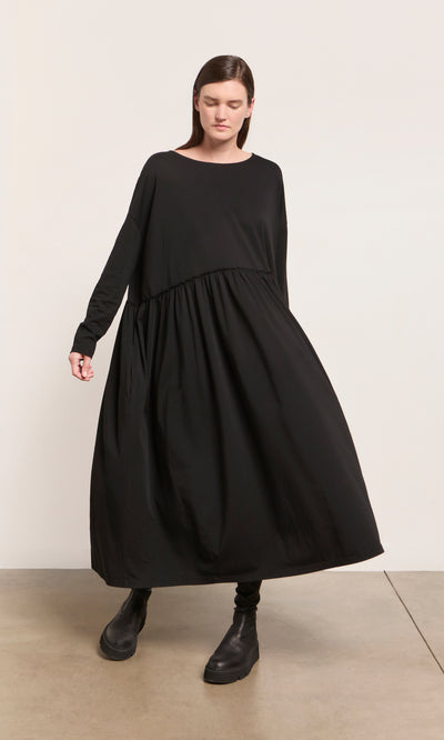 Plümo  Woman in the Kobke Dress and boots stands on a beige floor, embodying effortless Danish design style.
