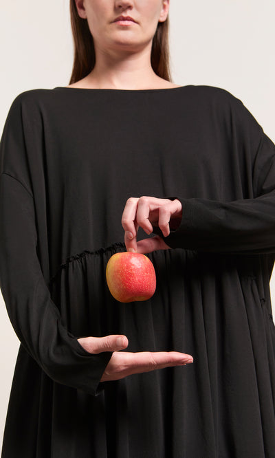 Plümo  Woman wearing the Kobke Dress, Danish design in black, holding a red apple against a plain background.