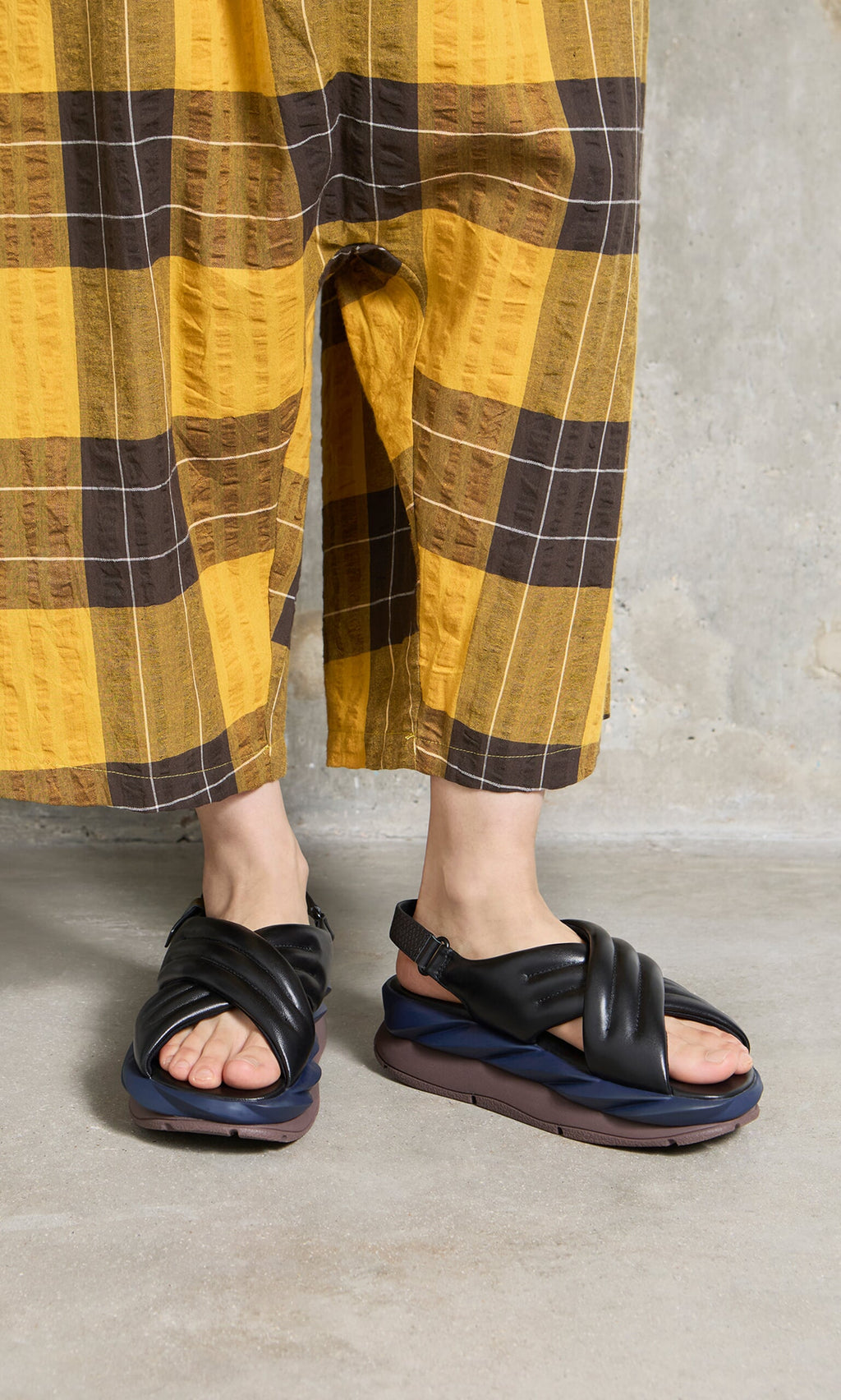 Plümo- Person in yellow plaid pants wearing Korra Sandals with cushioned insoles, standing on a concrete floor.