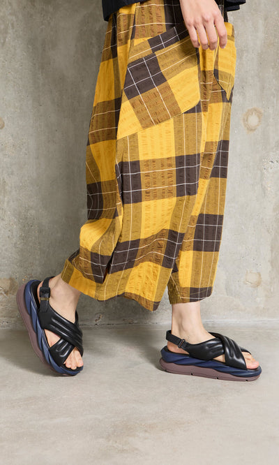 Plümo- Person in yellow and brown plaid pants walks on gray concrete floor wearing Korra Sandals.
