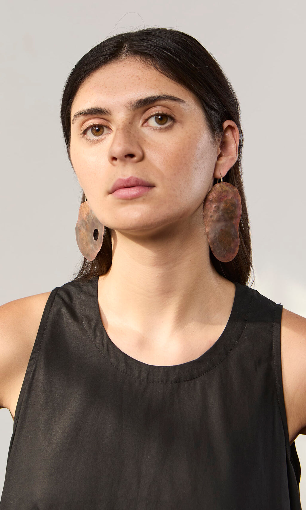 Plümo- Woman with long dark hair wearing a sleeveless black top and bold, handmade Large Chroma Earrings.