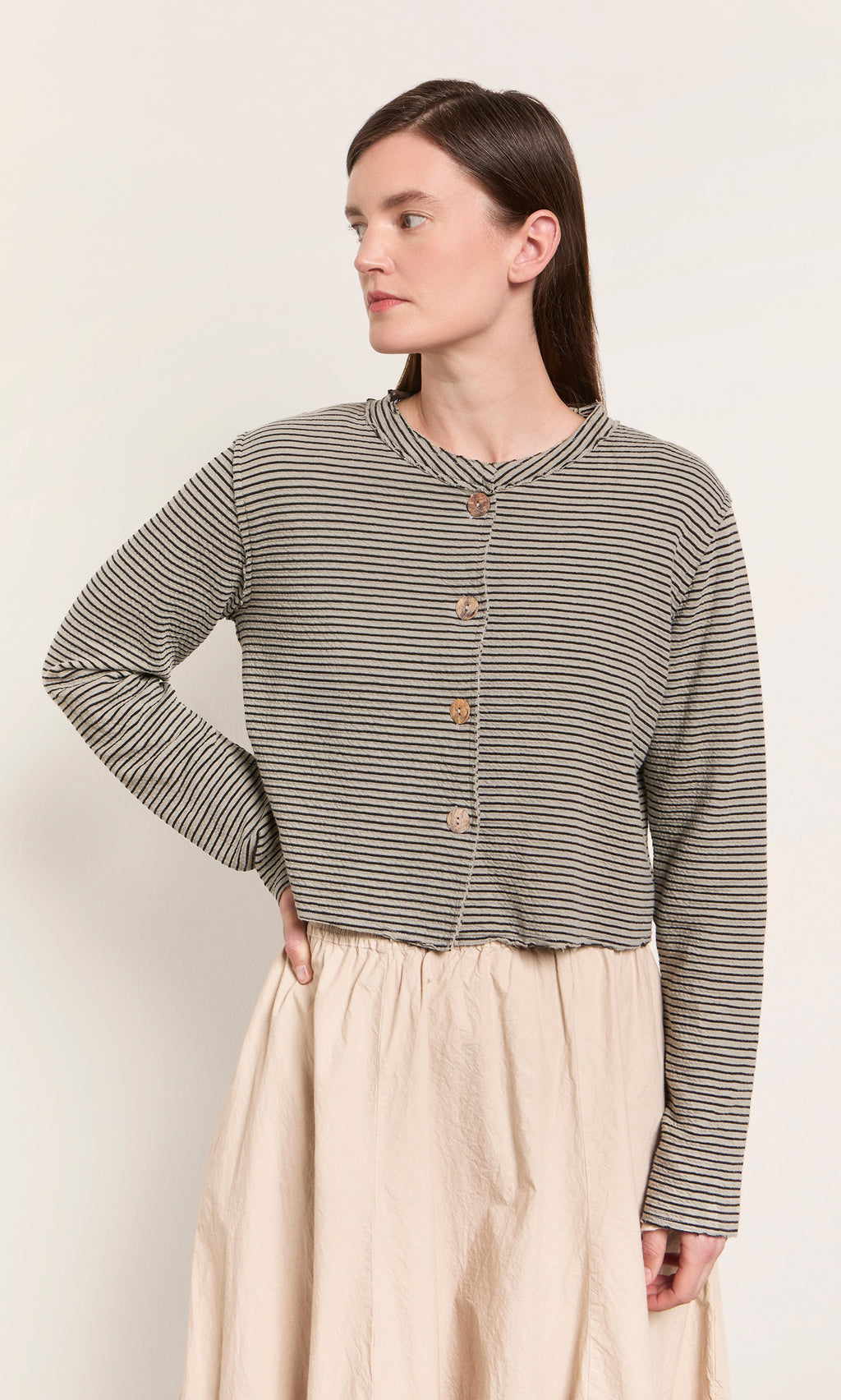 Plümo  Woman wears the Lavelle Top, a striped button-up, with a light beige skirt—made in the USA, hand on hip.