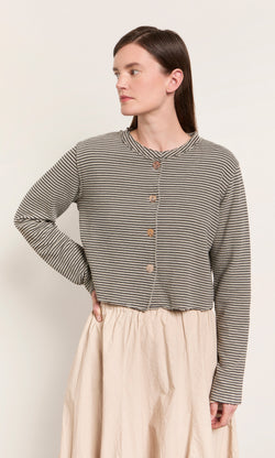 Plümo  Woman wears the Lavelle Top, a striped button-up, with a light beige skirt—made in the USA, hand on hip.