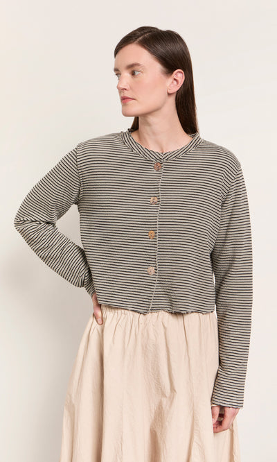 Plümo  Woman wears the Lavelle Top, a striped button-up, with a light beige skirt—made in the USA, hand on hip.