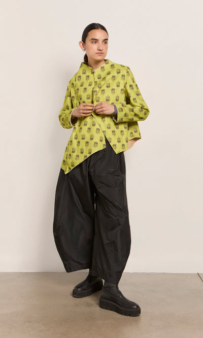Plümo  Person in a yellow shirt, black wide-leg pants, and the Leandra Jacket stands against a light wall.
