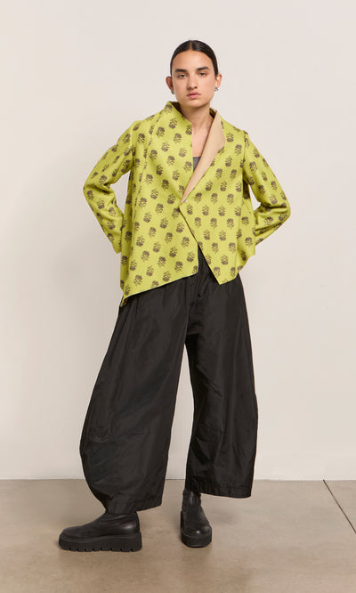 Plümo  Person in a lime green Leandra Jacket, black wide-leg pants, and platform boots stands against a plain backdrop.