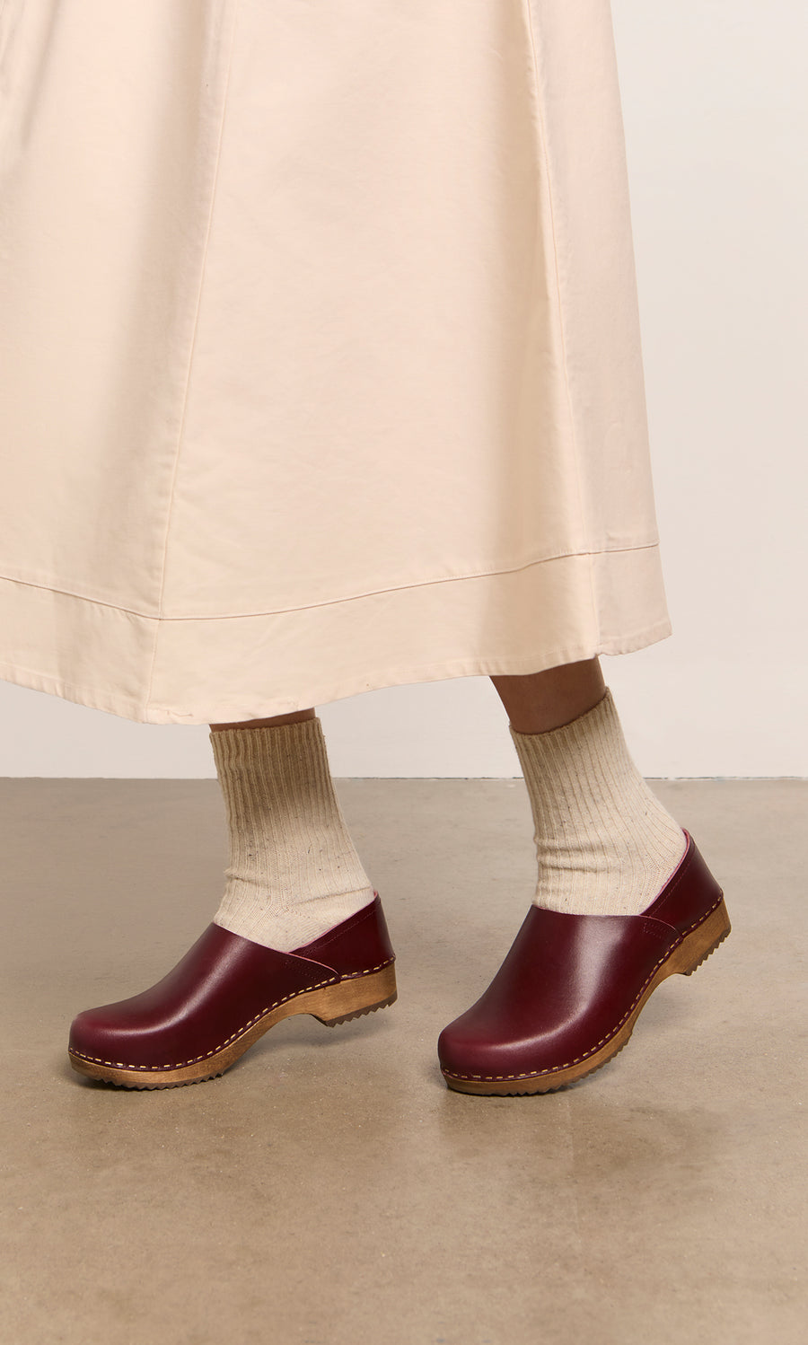 Plümo  Person wearing cream socks and Low Jord Clogs with a cream skirt, standing on a light brown floor.