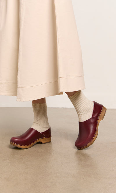 Plümo  Wearing cream socks and Low Jord Clogs, a person stands on a tan floor in a light beige midi-length skirt.