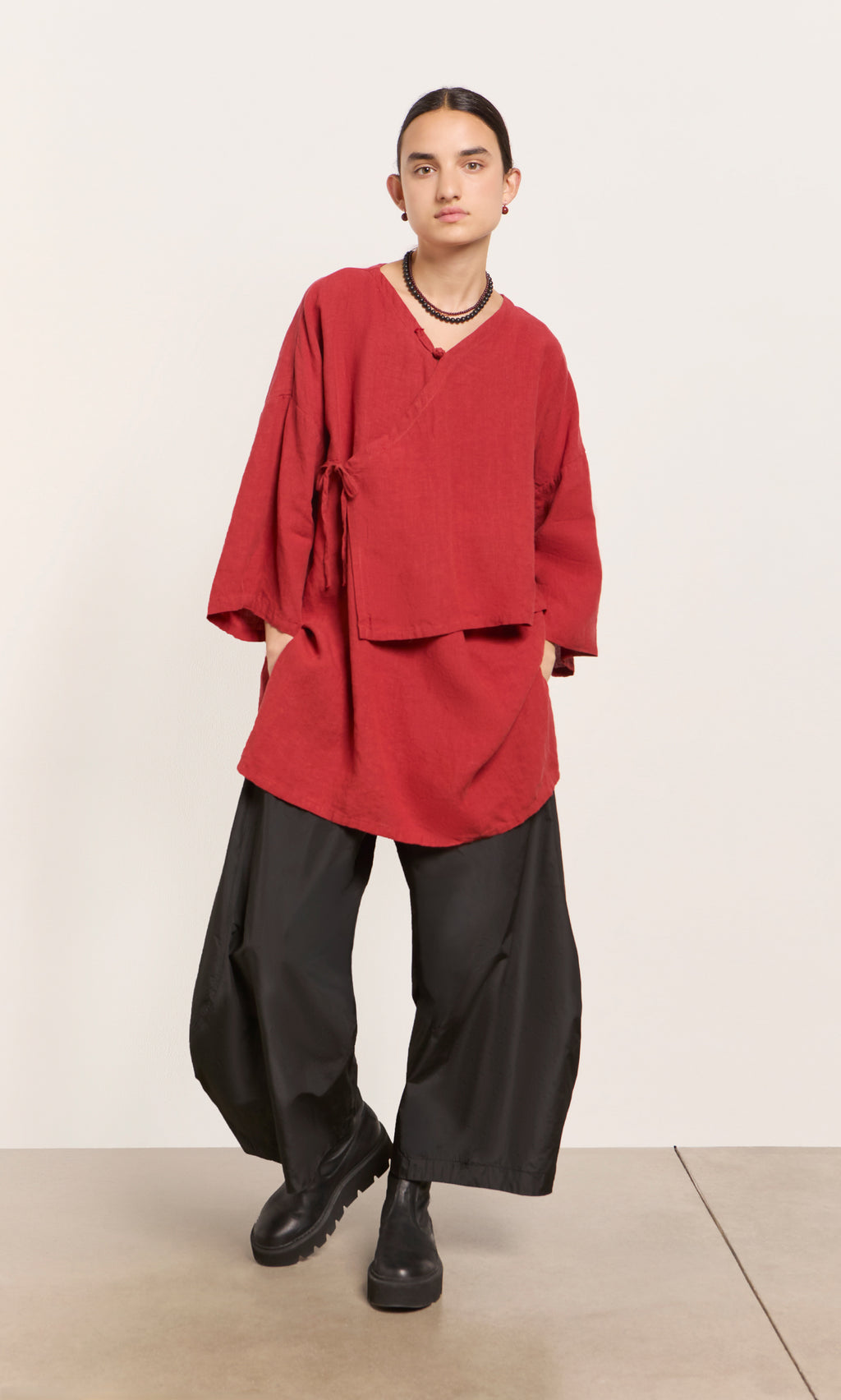 Plümo  Person wears a poppy red Leila tunic, wide black pants, and black boots against a plain background.
