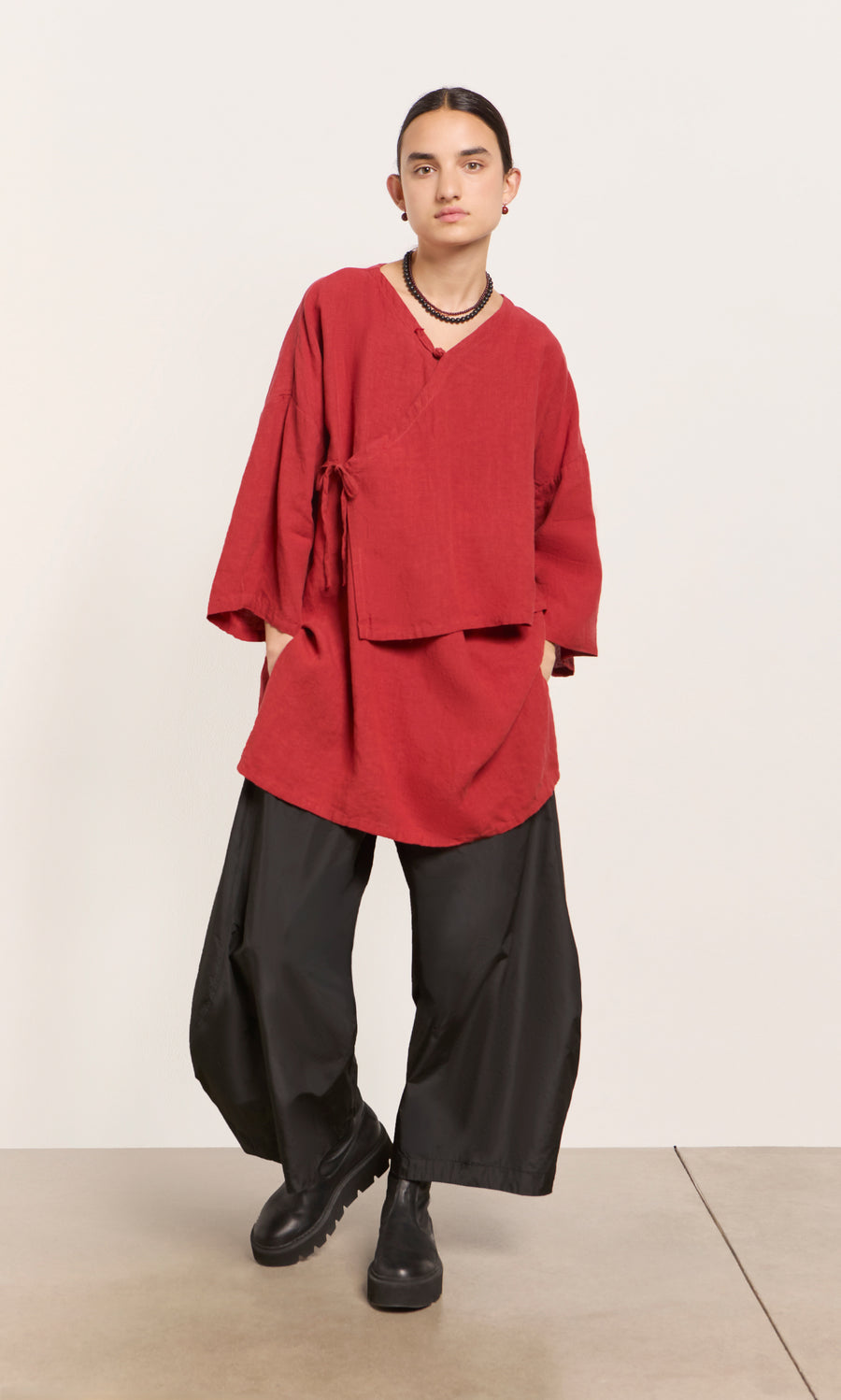 Plümo  Person wears a poppy red Leila tunic, wide black pants, and black boots against a plain background.