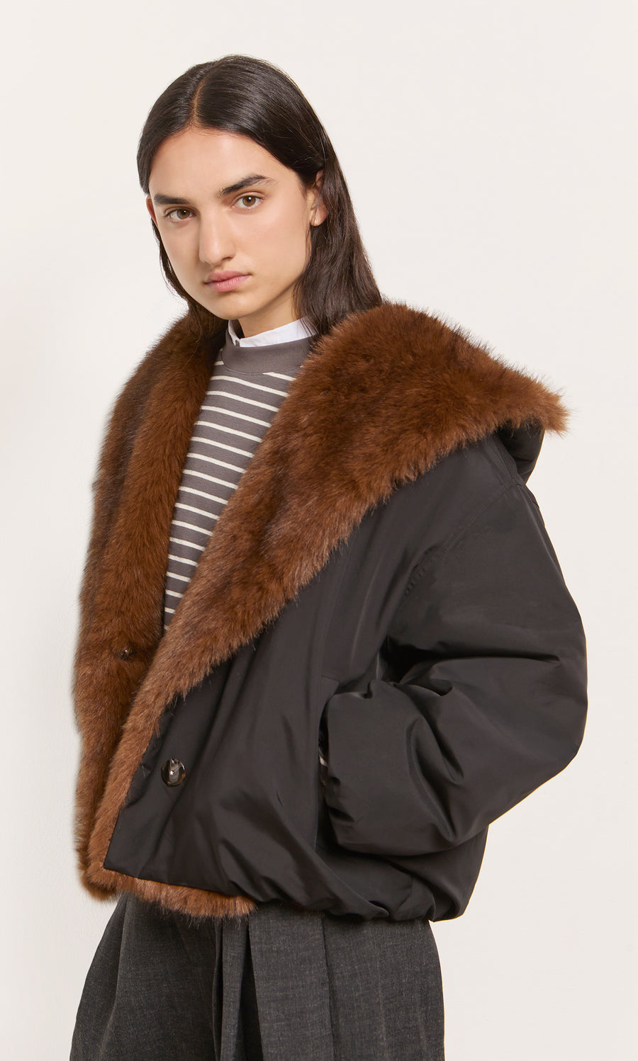 Plümo  Person wearing a Lenz Parka in acorn brown with faux fur trim and oversized hood, standing by a plain backdrop.