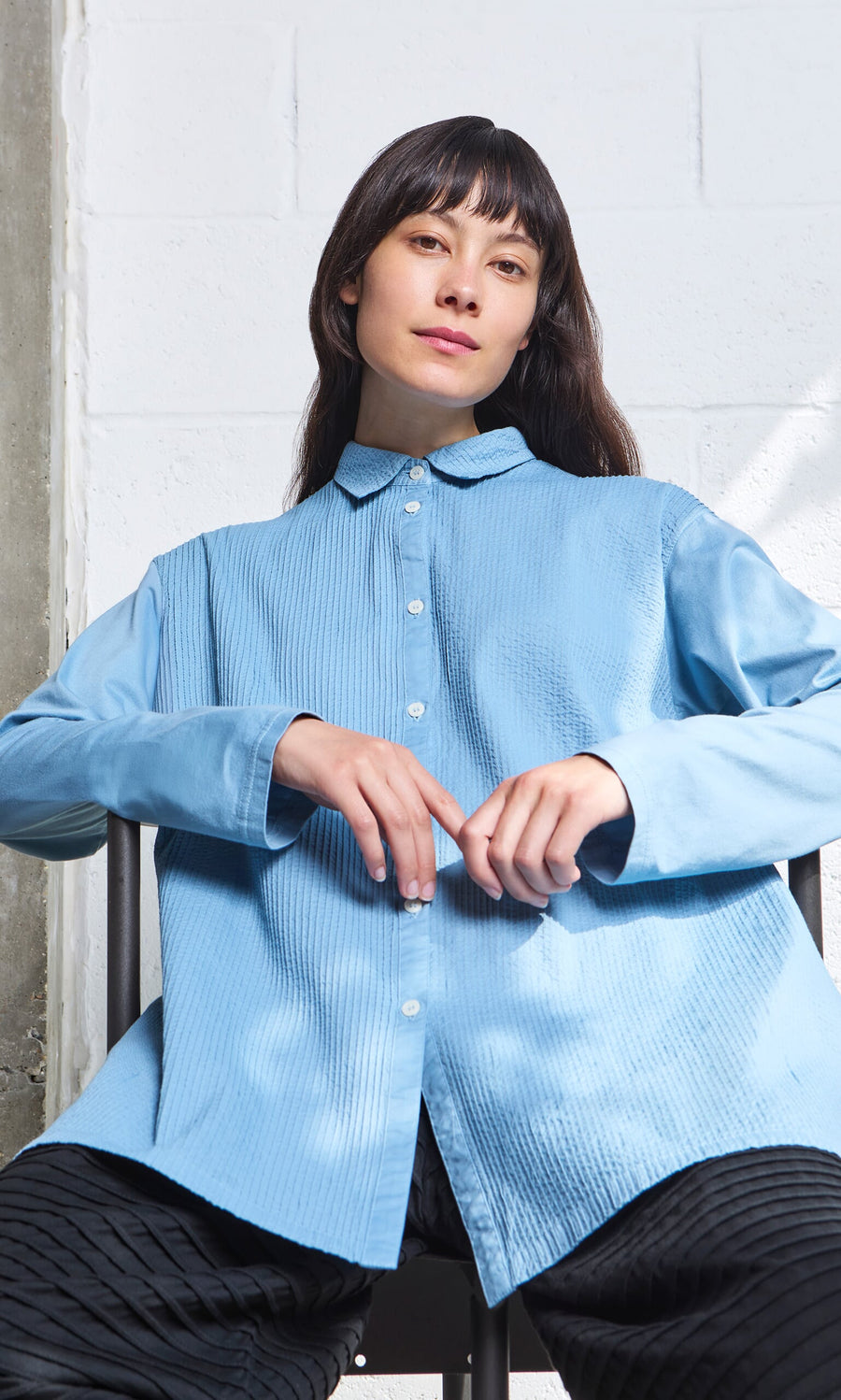 Plümo- Woman with long dark hair wears the Leung Shirt, a pintucked cotton Japanese tunic by Yacco Maricard, facing the camera.