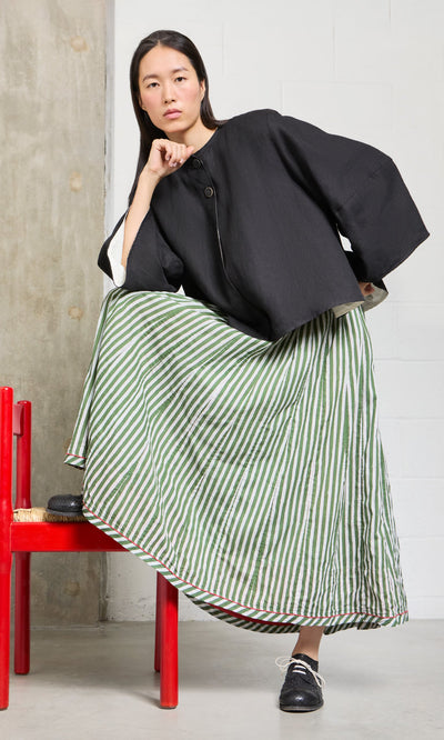 Plümo- A person poses on a red chair, wearing a black jacket and the Lilia Skirt with green-and-white stripes.