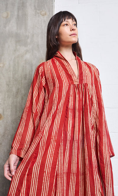 Plümo- Woman in a loose-fitting Lina Stripe Dress stands against a textured wall, looking upwards.
