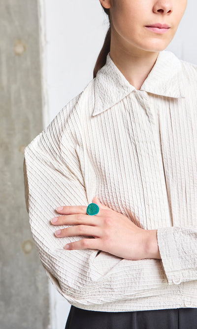 Plümo- Woman in a textured white blouse, arms crossed, wearing the bold Lowen Ring made from recycled silver.