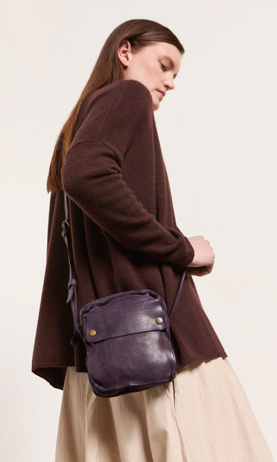 Plümo  Woman in brown sweater, beige skirt, with a deep purple Loyd Bag, looking off to the side.