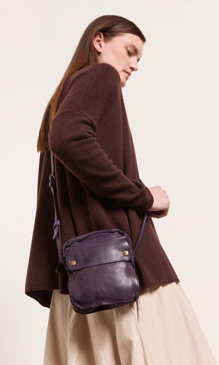 Plümo  Woman in brown sweater, beige skirt, with a deep purple Loyd Bag, looking off to the side.