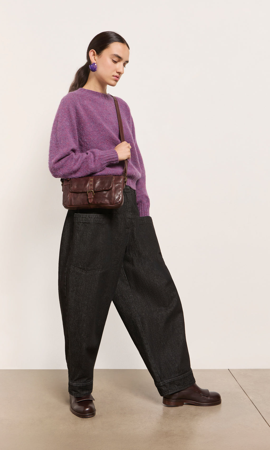 Plümo  Wearing a purple sweater, black pants, and brown shoes, a person carries the Luxton Bag while walking indoors.