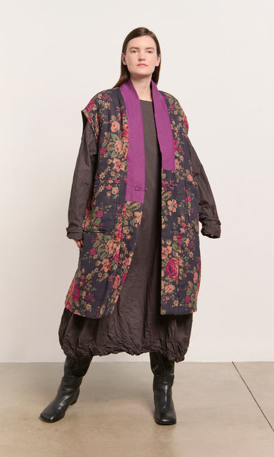 Plümo  Person wears a long brown dress, black boots, and the Manton Gilet against a plain background.