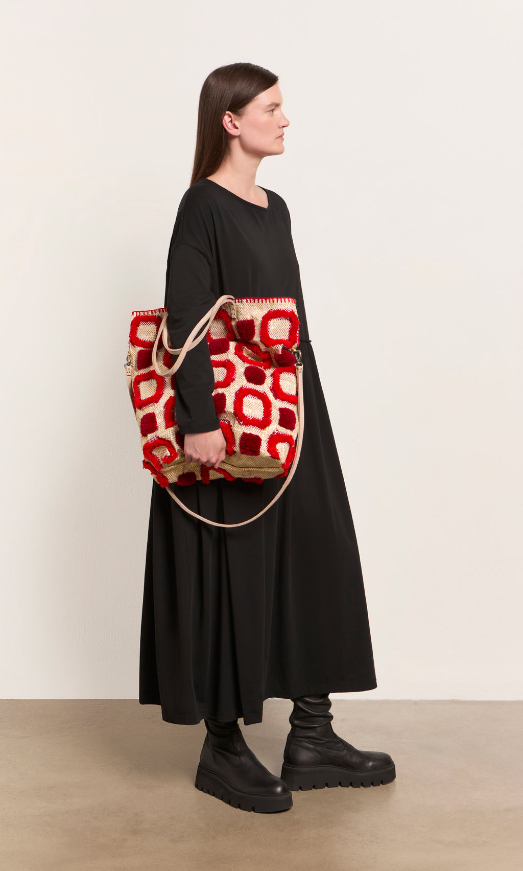 Plümo  Woman in a long black dress holds the Marakech Bag, an embroidered tote made in Morocco, against a plain background.