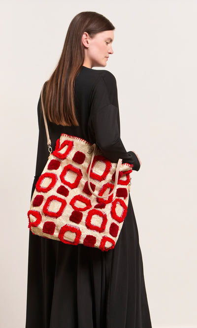 Plümo  Woman in a long black dress carrying the Marakech Bag, an embroidered tote with red and cream geometric patterns.