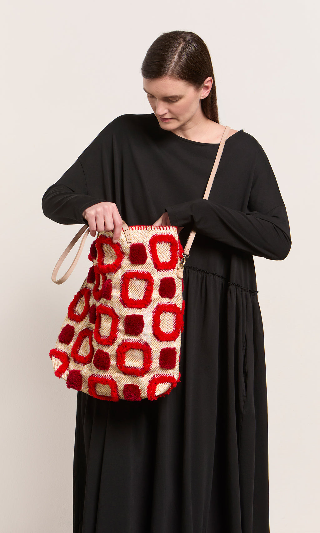 Plümo  Woman in a long black dress looks into the Marakech Bag, featuring red and beige straps, made in Morocco.
