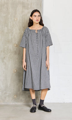 Plümo- Woman wears the Marin Dress - Plaid, a loose black-and-white short-sleeve dress made in London, with black shoes.