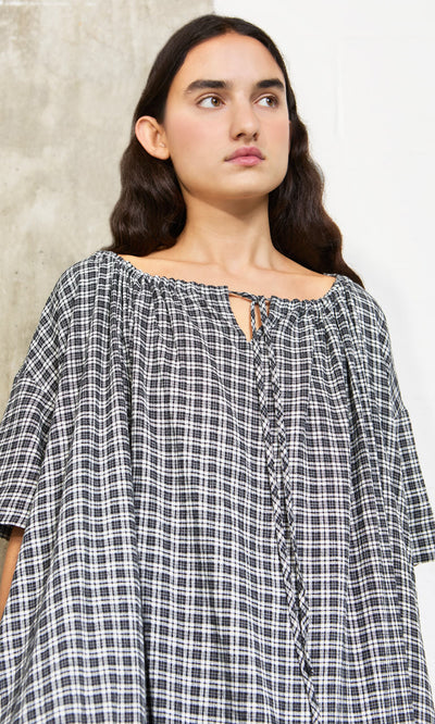 Plümo- Woman with long dark hair wears the Marin Dress - Plaid, a sustainable hemp piece made in London, against a pale backdrop.