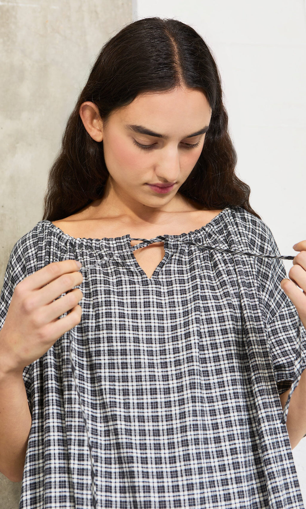 Plümo- A woman with long dark hair ties the neckline of the Marin Dress - Plaid, made from sustainable hemp.