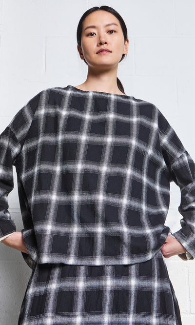 Plümo- Woman in the Italian-made Gifford Blouse, featuring a monochrome plaid design, stands confidently by a white wall.