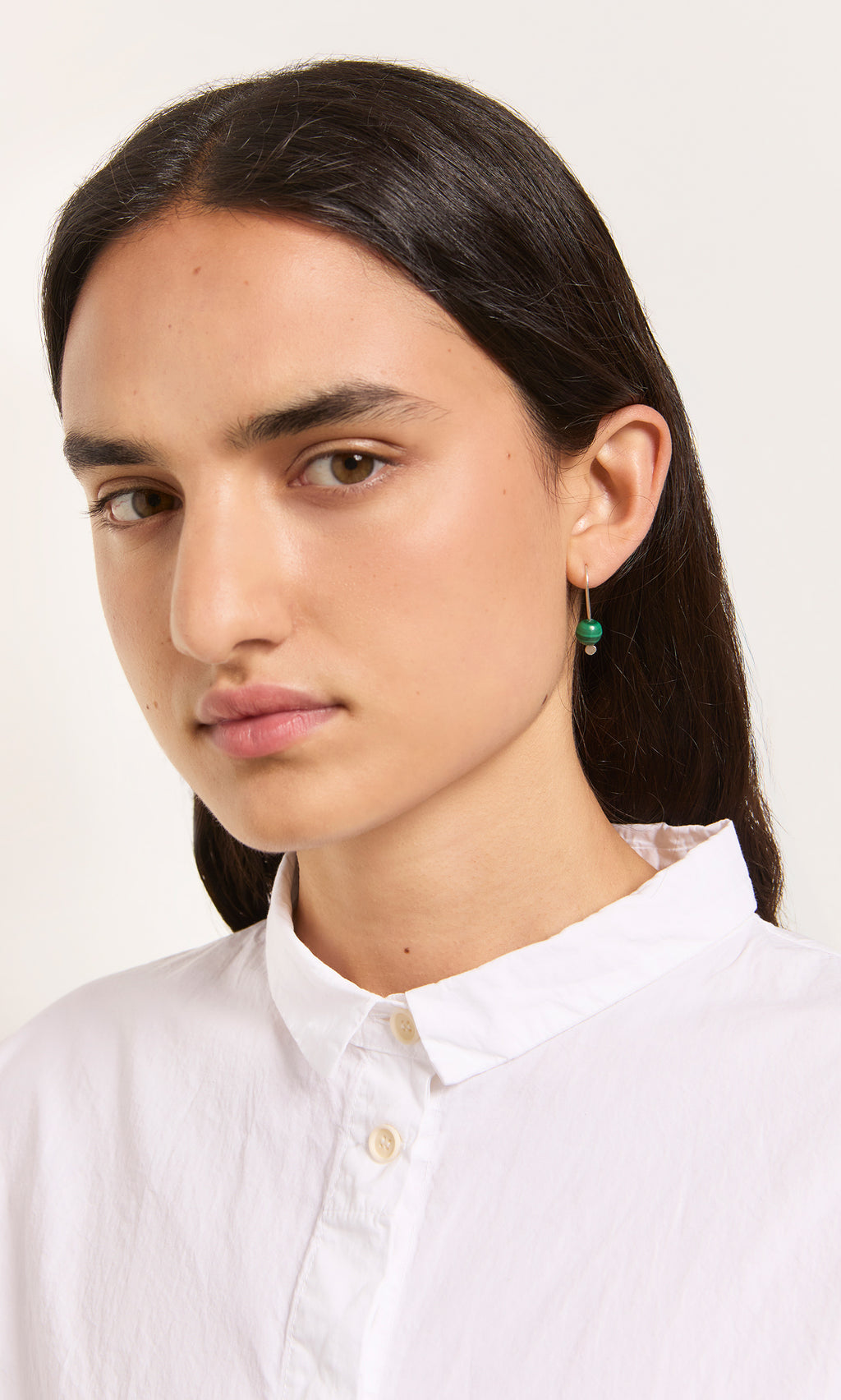 Plümo  Woman with long dark hair, white shirt, and Karli Earrings looks at camera—unique gemstone jewelry shines.