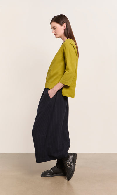 Plümo  Woman in a Moss Top - Corduroy and wide black pants stands sideways, hands in pockets.