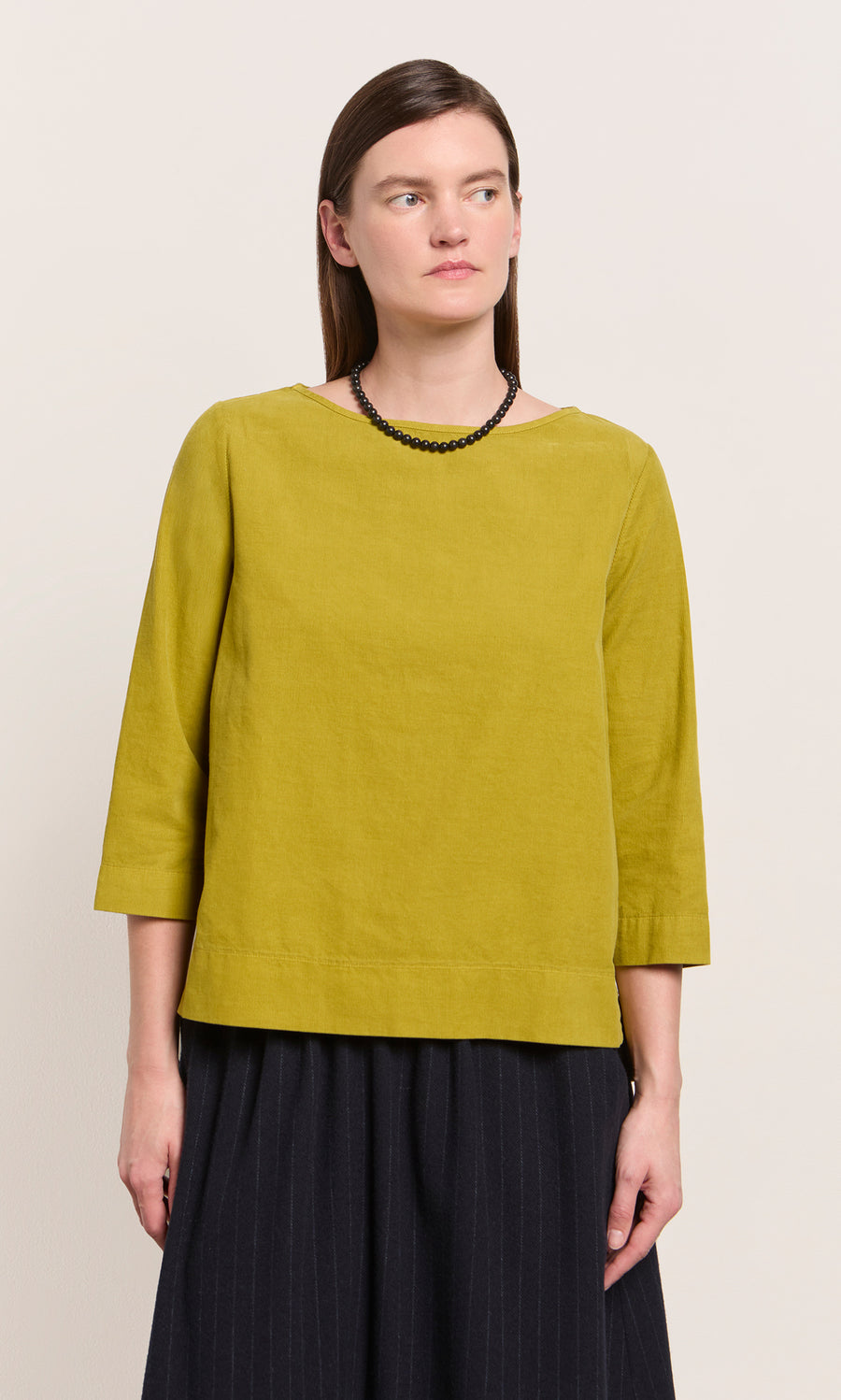 Plümo  Woman in a moss green Moss Top - Corduroy with a relaxed fit, black necklace, and black skirt.