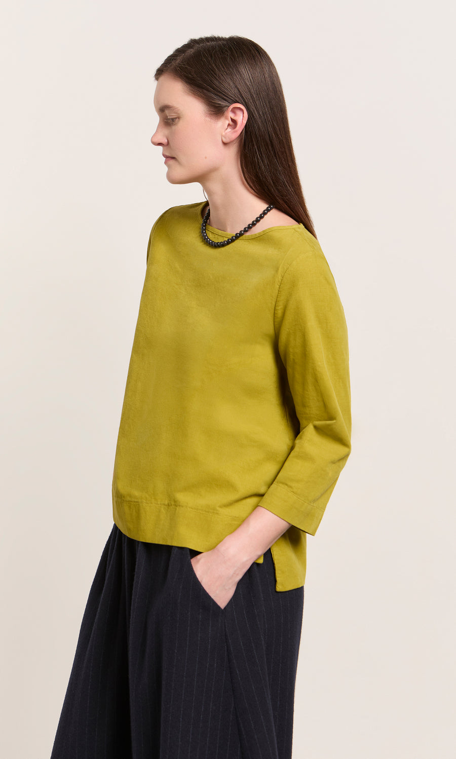 Plümo  Woman in Moss Top – Corduroy, relaxed fit, moss green, 3/4 sleeves, black necklace, standing sideways.