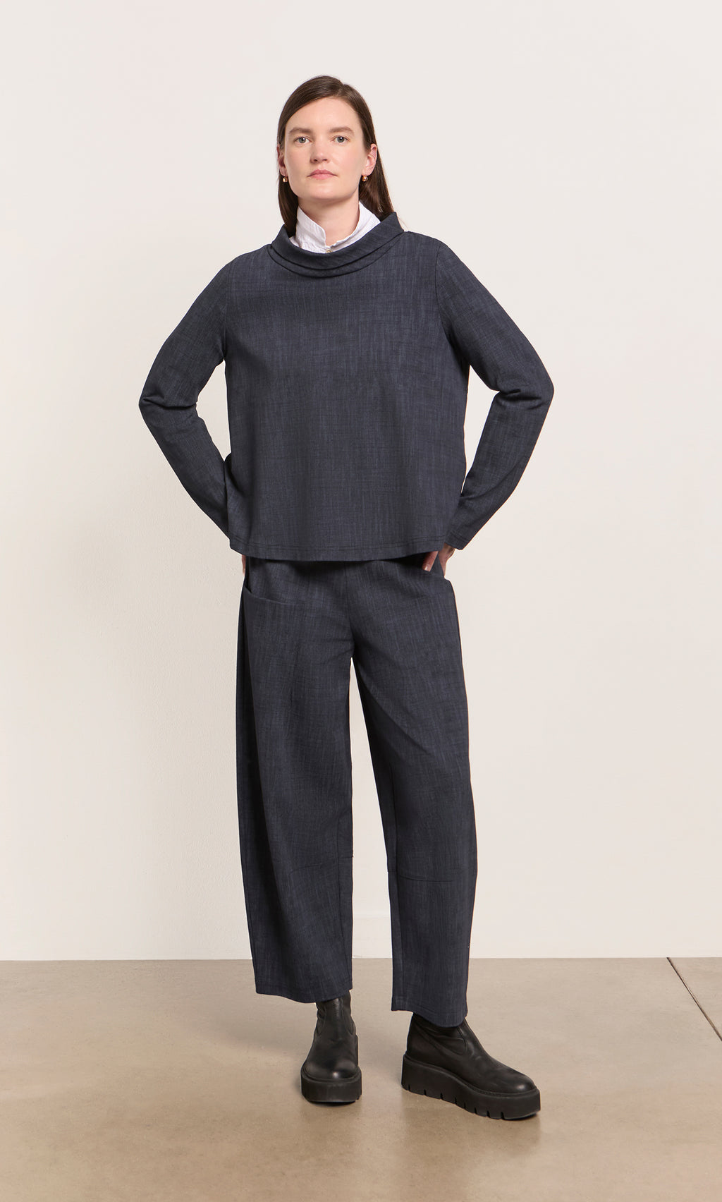 Plümo  Person wearing Cowl Blouse - Navy, white collar peeking out, hands in pockets, standing on a light floor.