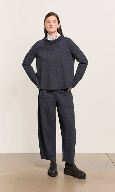 Plümo  Person wearing Cowl Blouse - Navy, white collar peeking out, hands in pockets, standing on a light floor.