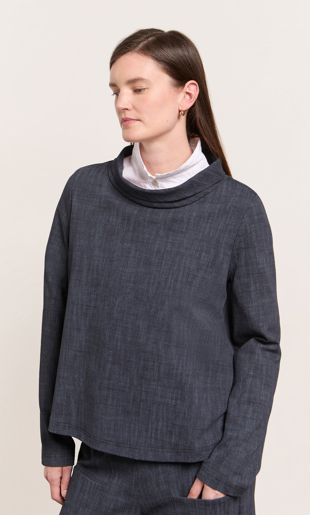 Plümo  A woman in the Cowl Blouse - Navy stands, eyes closed, against a plain background wearing a white shirt underneath.