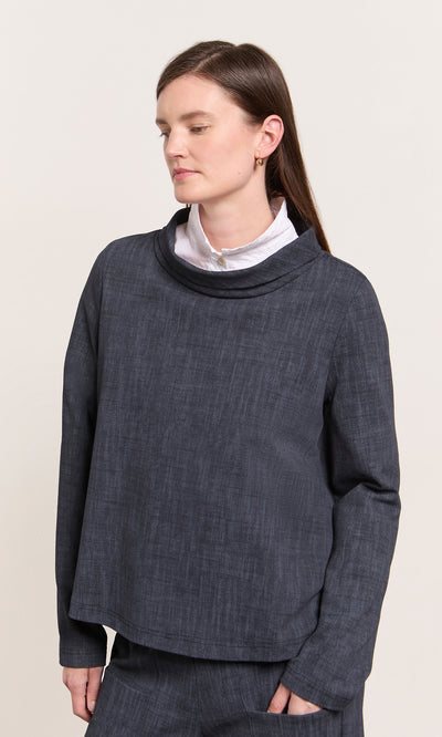 Plümo  A woman in the Cowl Blouse - Navy stands, eyes closed, against a plain background wearing a white shirt underneath.