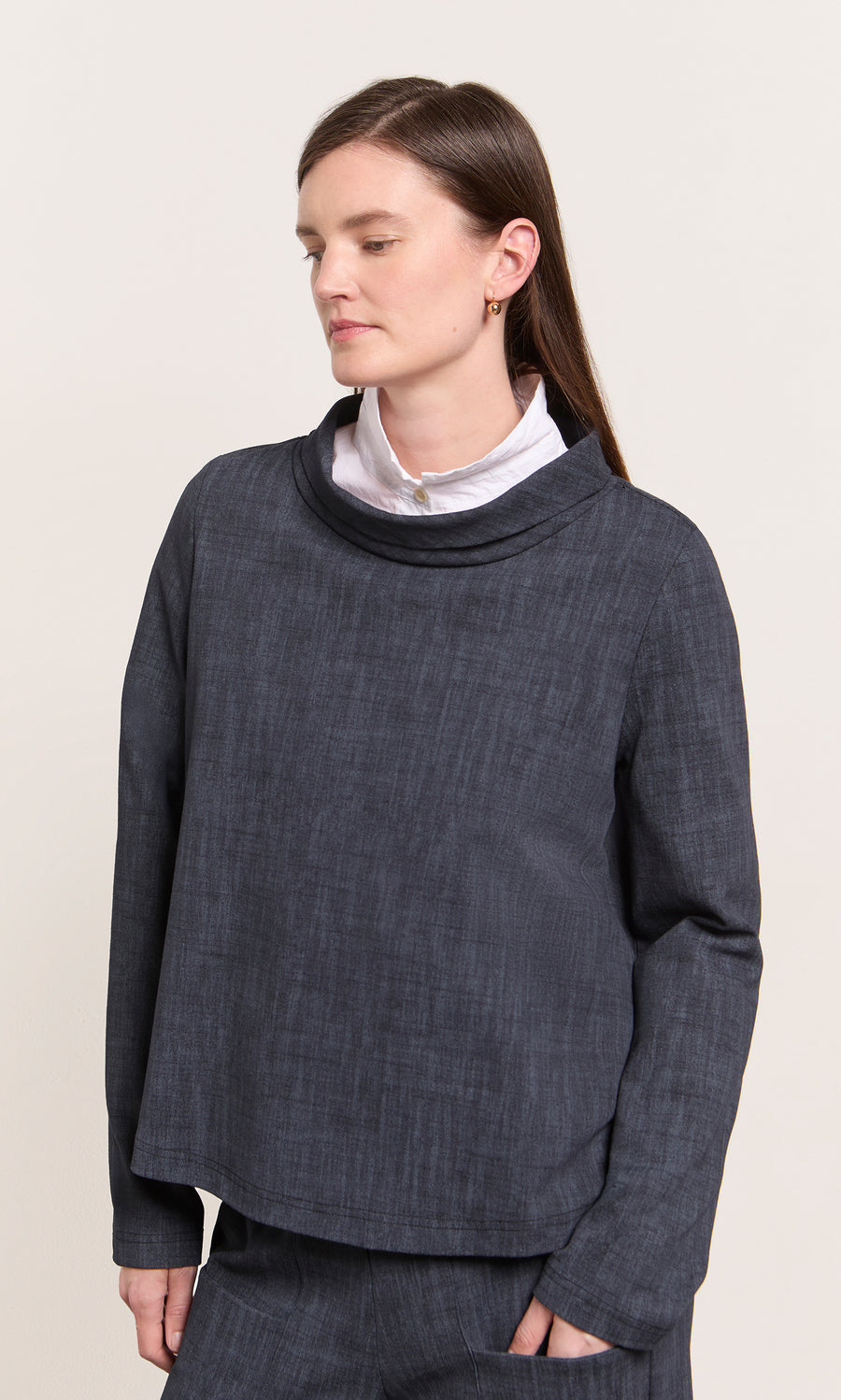 Plümo  A woman in the Cowl Blouse - Navy stands, eyes closed, against a plain background wearing a white shirt underneath.