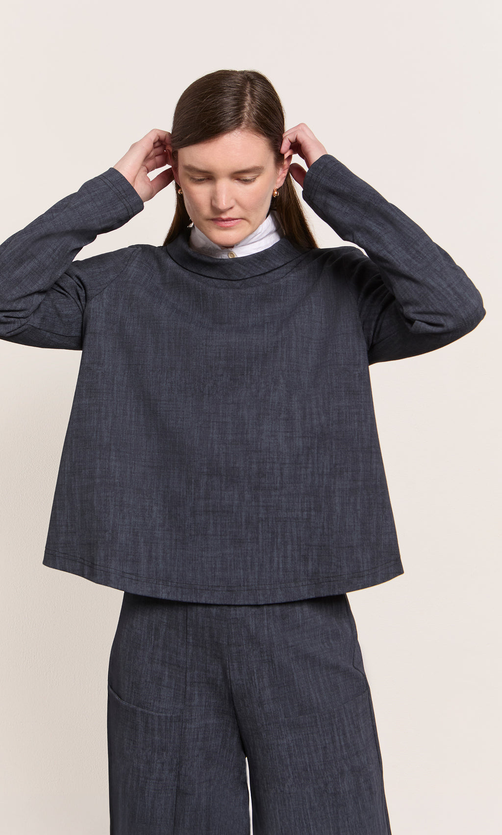 Plümo  Person adjusting hair, wearing Cowl Blouse - Navy and matching pants, standing against a plain background.