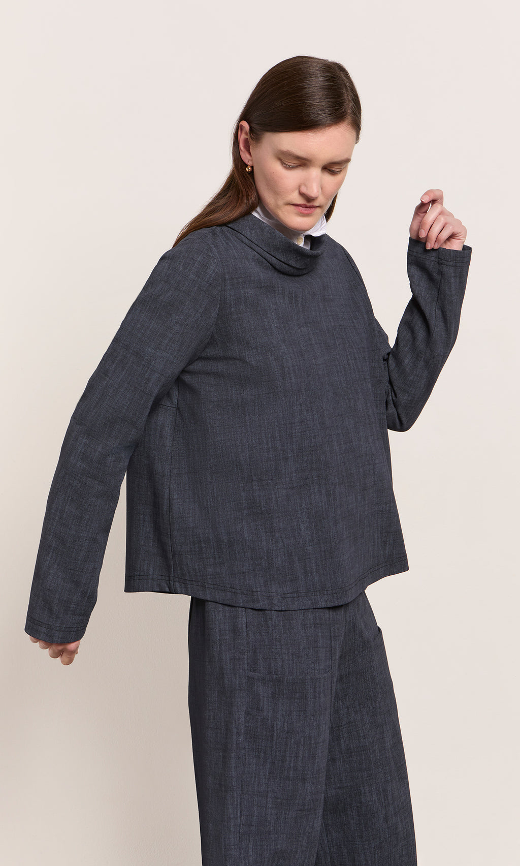 Plümo  Woman in a navy Cowl Blouse with scoop hem and matching pants, looking slightly downward.